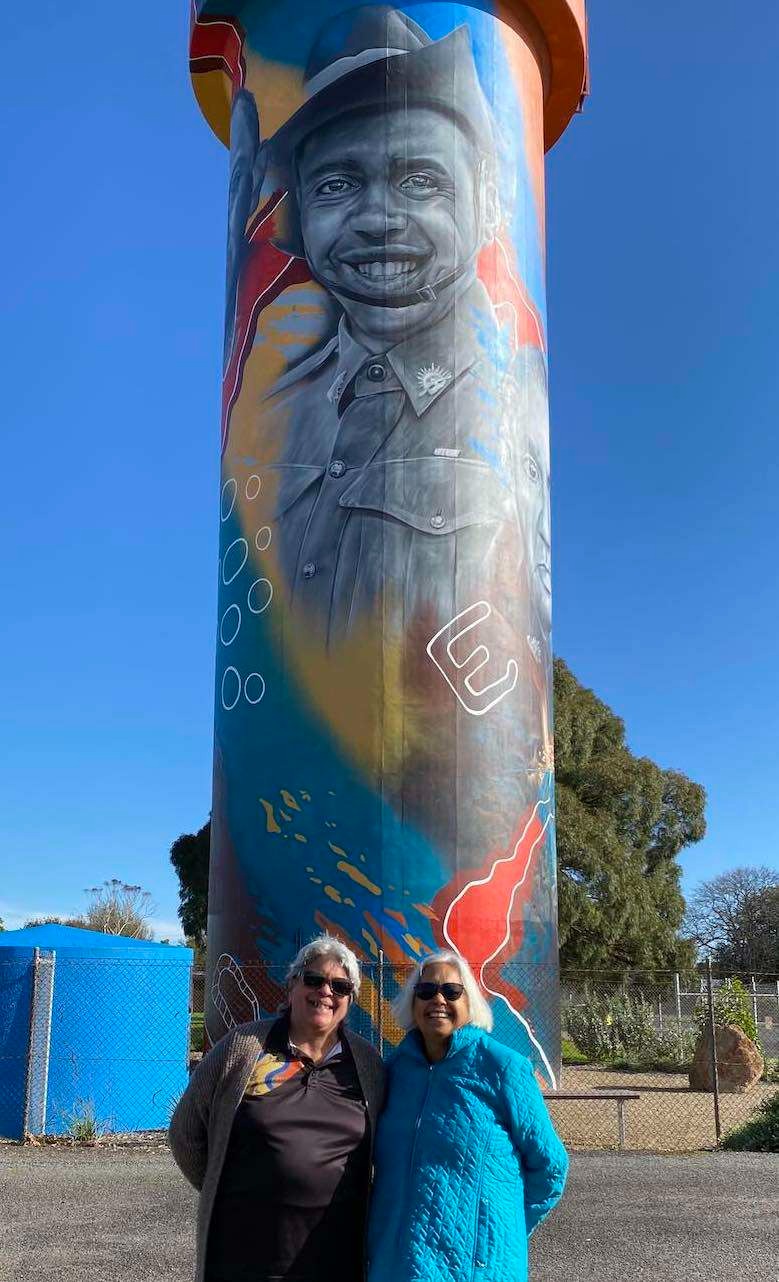 Hilary Saunders and Glenda Humes with the water tower in Heywood, Victoria, depicting the image of their father Captain Reginald Saunders MBE. (Read more here).